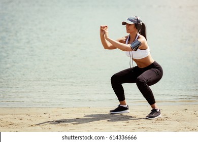 Young muscular fitness woman doing squats exercise by the river.