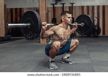 Young muscular male bodybuilder doing squats with a barbell on his shoulders in a modern health club. Bodybuilding and Fitness