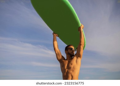 Young Muscular Male Surfer Holding Surfboard Over Head And Looking Aside, Handsome Athletic Millennial Guy In Stylish Sunglasses Posing Over Sky Background, Enjoying Summer Surfing, Copy Space - Powered by Shutterstock