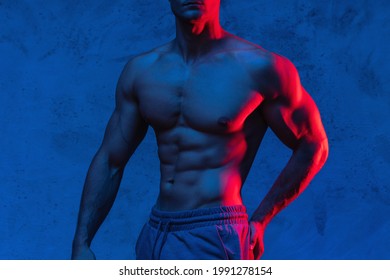 Young and muscular man bodybuilder is posing in the colorful neon light