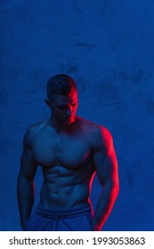 Young and muscular man bodybuilder is posing in the colorful neon light