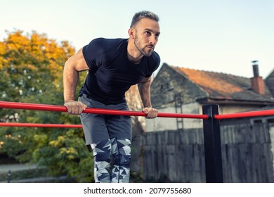 Young Muscular Man Doing Calisthenics Outside Lifting Himself Above The Bar, Street Gymnastics Concept