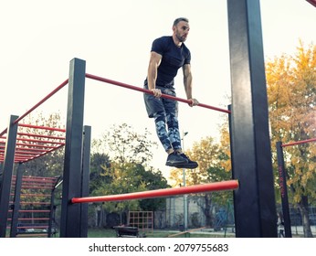 Young Muscular Man Doing Calisthenics Outside Lifting Himself Above The Bar, Street Gymnastics Concept