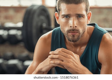 Young Muscular Man Resting In Gym While Looking At Camera. Portrait Of Competitive Sportsman At Wellness Center. Determined Sweaty Guy Taking A Break After Working Out Session With Copy Space.