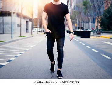 Young muscular man wearing black tshirt and jeans walking on the streets of the modern city. Blurred background. Hotizontal mockup
