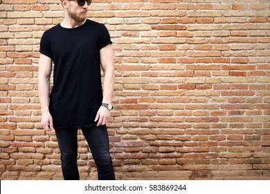 Young Muscular Man Wearing Black Tshirt,sunglasses And Jeans Posing Outside. Empty Brown Grunge Brick Wall On The Background. Hotizontal Mockup