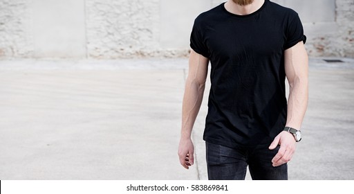 Young muscular man wearing black tshirt and jeans walking on the urban district. Blurred background. Hotizontal wide mockup