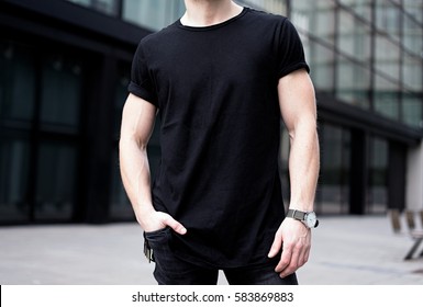 Young Muscular Man Wearing Black Tshirt And Jeans Posing In Center Of Modern City. Blurred Background. Hotizontal Mockup