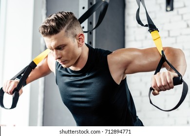 Young Muscular Sportsman Training With Trx Resistance Bands In Gym  