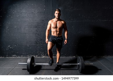 Young Muscular Sweaty Fit Man With Big Muscles Standing Above Heavy Barbell Weight After Cross Training Workout In The Gym Dark Image Real People