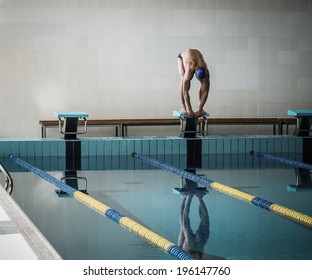 Young muscular swimmer in low position on starting block in a swimming pool
