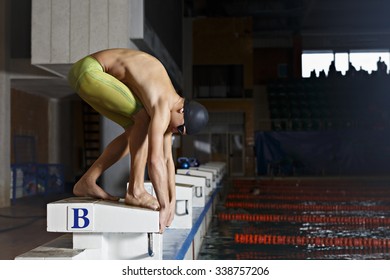 Young muscular swimmer in low position on starting block in a swimming pool - Powered by Shutterstock