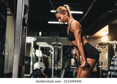 A young muscular woman is doing training on machine for her triceps muscle at the gym.