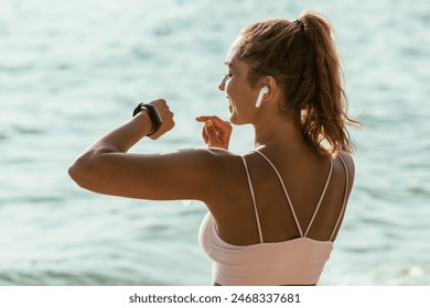 A young muscular woman is looking at smartwatch and preparing to jogging on the beach, during summer holiday. - Powered by Shutterstock