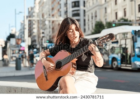 young music student sitting in the city playing the acoustic guitar.