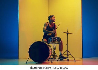 Young musician with drums performing on yellow background in neon light. Concept of music, hobby, festival, entertainment, emotions. Joyful, inspired drummer. Colorful portrait of artist. - Powered by Shutterstock