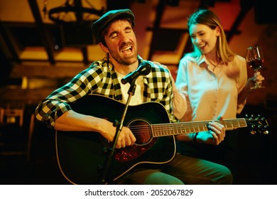 Young musician playing acoustic guitar and singing in a bar at night.  - Powered by Shutterstock