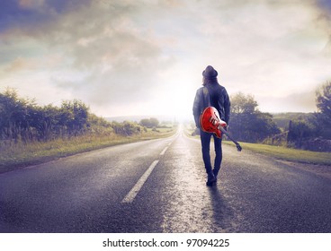 Young musician walking on a countryside road with a guitar on his shoulder - Powered by Shutterstock