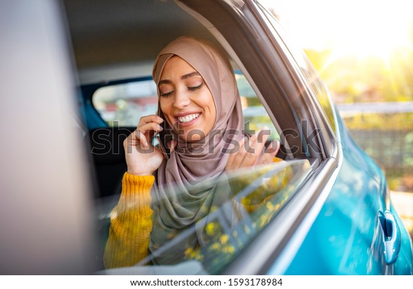 Young muslim business woman sitting in\
car. Muslim girl with scarf on her head sitting in the car and\
talking on the phone. Muslim business woman in car.\
