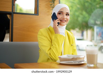 Young Muslim Businesswoman In Headscarf Sitting In Cafe And Talking On The Phone