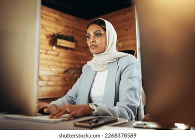 Young Muslim businesswoman working on a computer in a modern office. Ethnic businesswoman wearing a hijab in an inclusive workplace. - Powered by Shutterstock