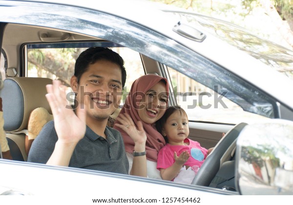 young muslim family , transport, leisure, road trip\
and people concept - happy man, woman and little girl inside car\
waving at camera ready for traveling in a car looking out windows\
at sunny day