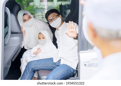 Young Muslim Family Wearing Face Mask While Waving Hands At Their Grandparents After Eid Mubarak Celebration And Sitting On Car Backseat