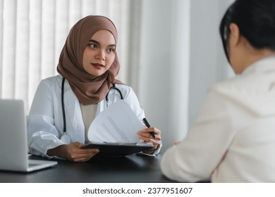 Young muslim female doctor in brown hijab headscarf having appointment consulting female patient in modern clinic hospital. Medical healthcare concept - Powered by Shutterstock