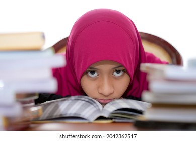 A Young Muslim Female Teen With Hijab Reading A Book While Staring At The Camera, Isolated On White Background