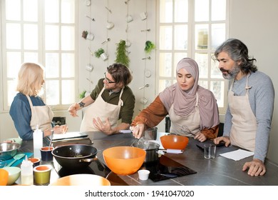 Young Muslim Female Trainee In Hijab Holding Whisker Over Pan With Water On Electric Stove While Cooking At Masterclass Among Other Learners