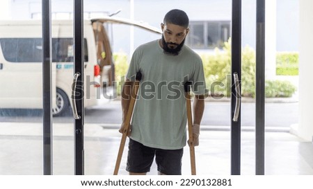 Young Muslim man with his crutches walking into a hospital reception counter. Bearded man with walking sticks.