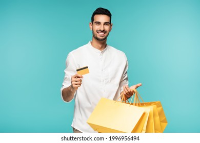 Young Muslim Man Holding Credit Card And Shopping Bags Isolated On Blue