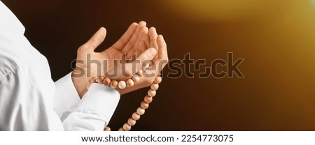 Young Muslim man with prayer beads on dark background, closeup