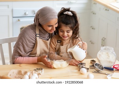 Young Muslim Mom Baking Together With Her Little Daughter In Kitchen. Cute Little Arab Girl Helping Mom To Prepare Dough, Adding Ingredients To Bowl, Islamic Family Having Fun While Cooking At Home