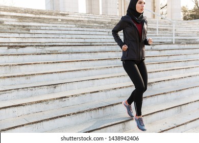 Young Muslim Sports Fitness Woman Dressed In Hijab And Dark Clothes Running Outdoors At The Street By Steps.