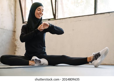 Young muslim sportswoman in hijab looking at smartwatch while working out indoors - Powered by Shutterstock