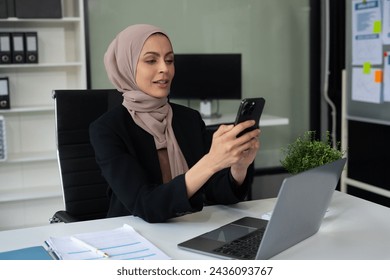 young muslim woman drinking coffee and checking email on tablet and laptop at her office desk. - Powered by Shutterstock