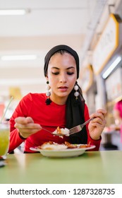 A Young Muslim Woman In A Hijab Head Scarf Eats Her Halal Nasi Lemak Lunch During The Day At A Table In A Hawker Center. 