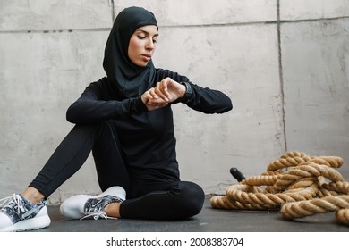 Young muslim woman in hijab looking at smartwatch while sitting on floor indoors - Powered by Shutterstock