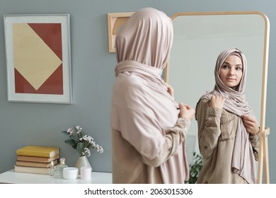 Young Muslim Woman In Hijab Looking In Large Mirror While Getting Dressed For Work In The Morning