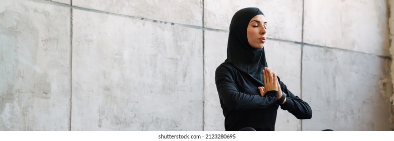 Young Muslim Woman In Hijab Meditating While Sitting On Fitness Mat Indoors