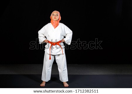 Young muslim woman in kimono and hijab in karate training over black background