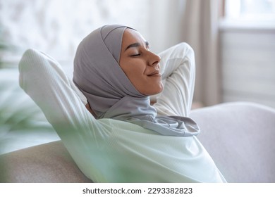 Young muslim woman resting at home with eyes closed hands behind head napping sitting on sofa, woman in hijab close up in living room. - Powered by Shutterstock