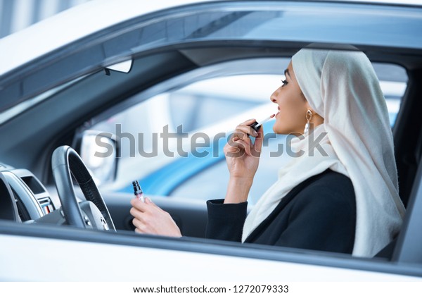 young\
muslim woman sitting in car and applying\
makeup