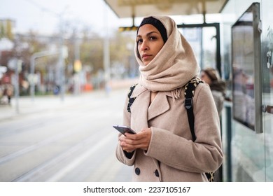 Young muslim woman with smartphone waiting for bus at city bus stop. - Powered by Shutterstock