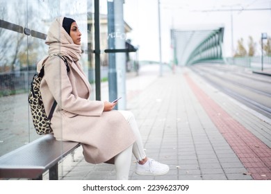 Young muslim woman waiting for tram at tram stop.