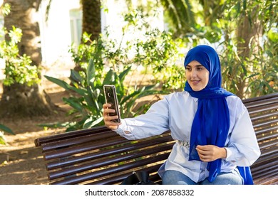 Young Muslim Woman Wearing Hijab Sitting On Park Bench Taking A Selfie