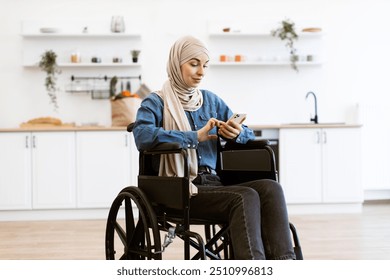 Young Muslim woman wearing hijab sitting in wheelchair using smartphone at home kitchen. Modern lifestyle, technology, and accessibility concept - Powered by Shutterstock