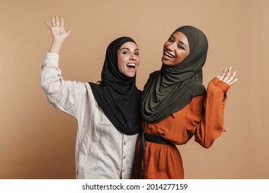 Young Muslim Women In Hijab Hugging And Laughing At Camera Isolated Over Beige Background