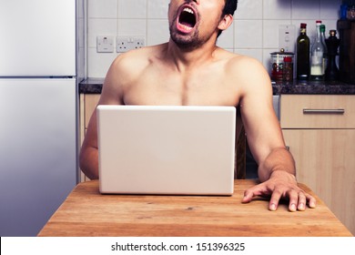 Young naked man watching pornography in his kitchen